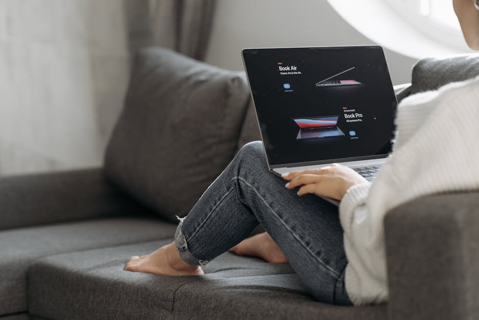 Woman sitting on a couch browsing laptops online. Perfect for online shopping or lifestyle contexts.
