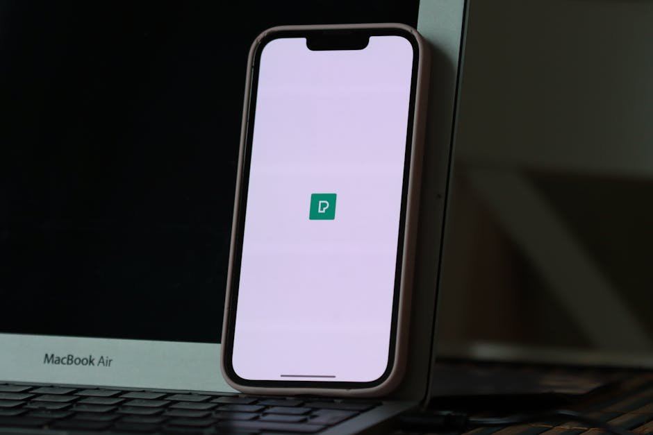 Smartphone resting against a laptop screen with app icon displayed, indoors.
