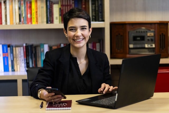 A woman smiles while working on a laptop.