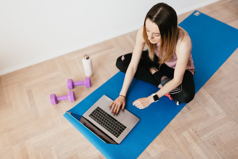 Young woman on yoga mat using laptop for online workout or relaxation.