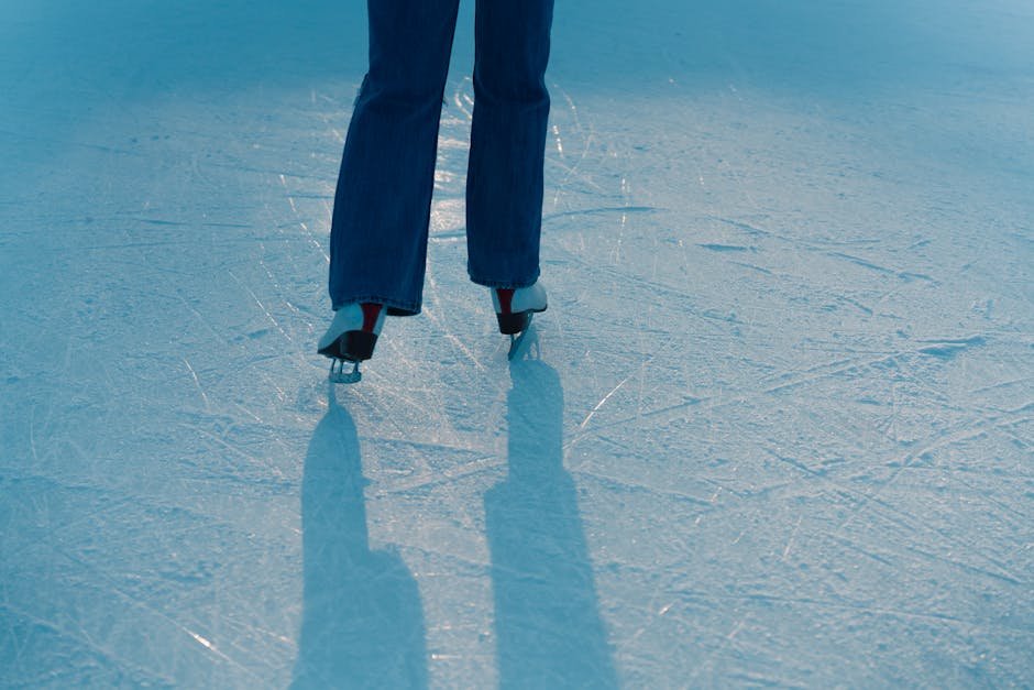Rear view of individual ice skating on a textured rink with shadows cast in sunlight.