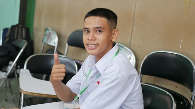 a young man sitting at a table giving a thumbs up