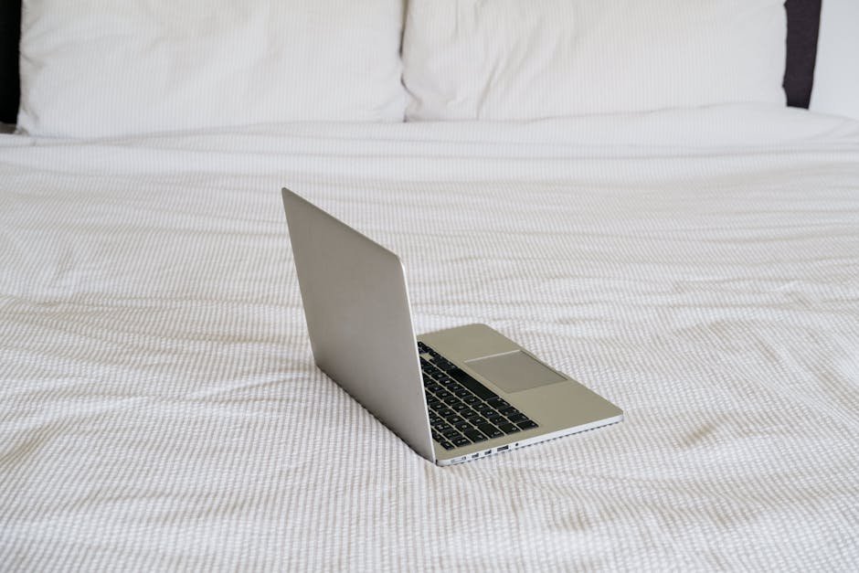 A sleek laptop sits open on a cozy bed, showcasing a minimalist and contemporary bedroom design.